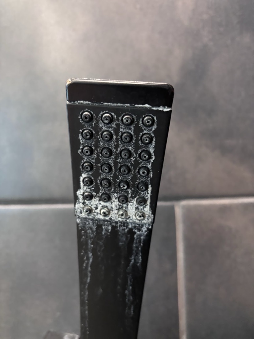 Calcium buildup removed from a black handheld shower head: before
