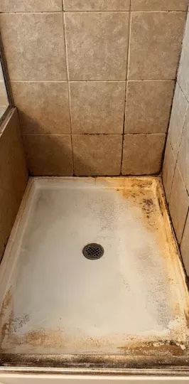 Rust and hard water stains removed from a shower pan: before
