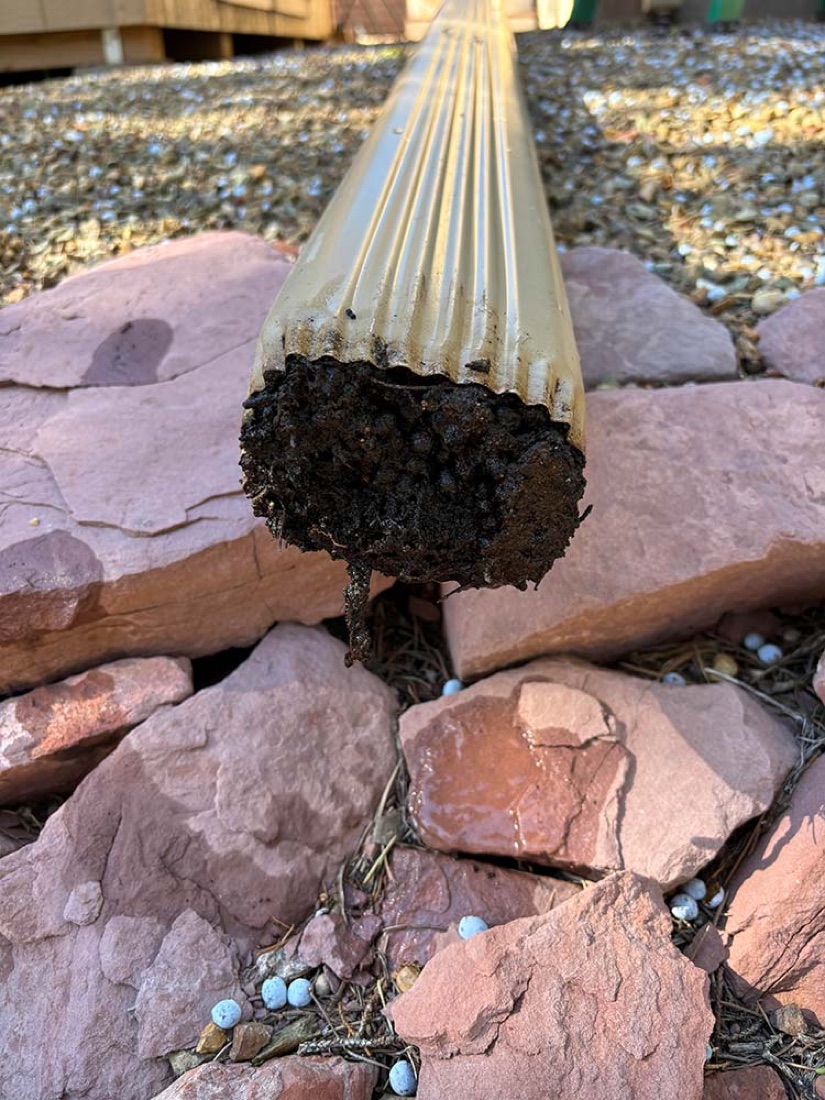 Downspout packed solid with mud and debris