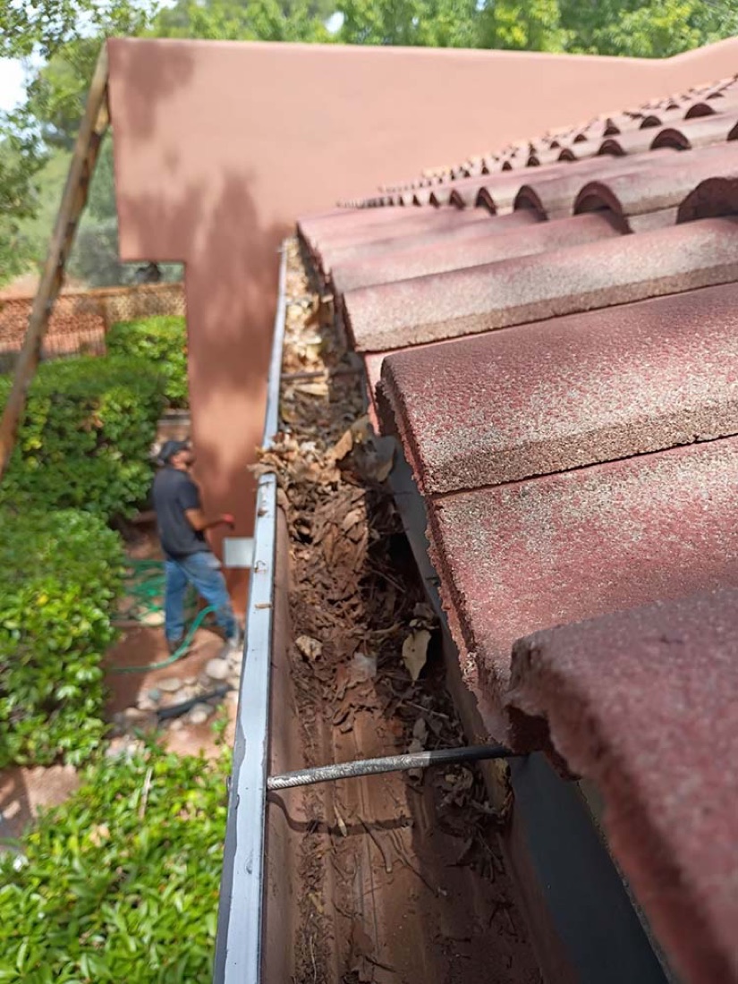 Leaves and debris filling a gutter under a tile roof