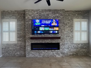 Stacked stone accent wall with a mounted TV, wood mantel and electric fireplace insert
