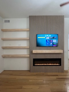 Wood slat accent wall with a TV, mantel and fireplace insert beside floating shelves