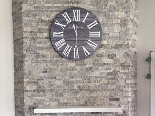 Oversized wall clock mounted on a stacked stone fireplace above the mantel