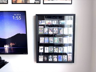 Wall-mounted sports card display case hung level beside a TV