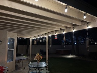 Bistro lights hung along the beams of a backyard patio cover at night