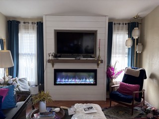 TV recessed into a shiplap wall above an electric fireplace and mantel