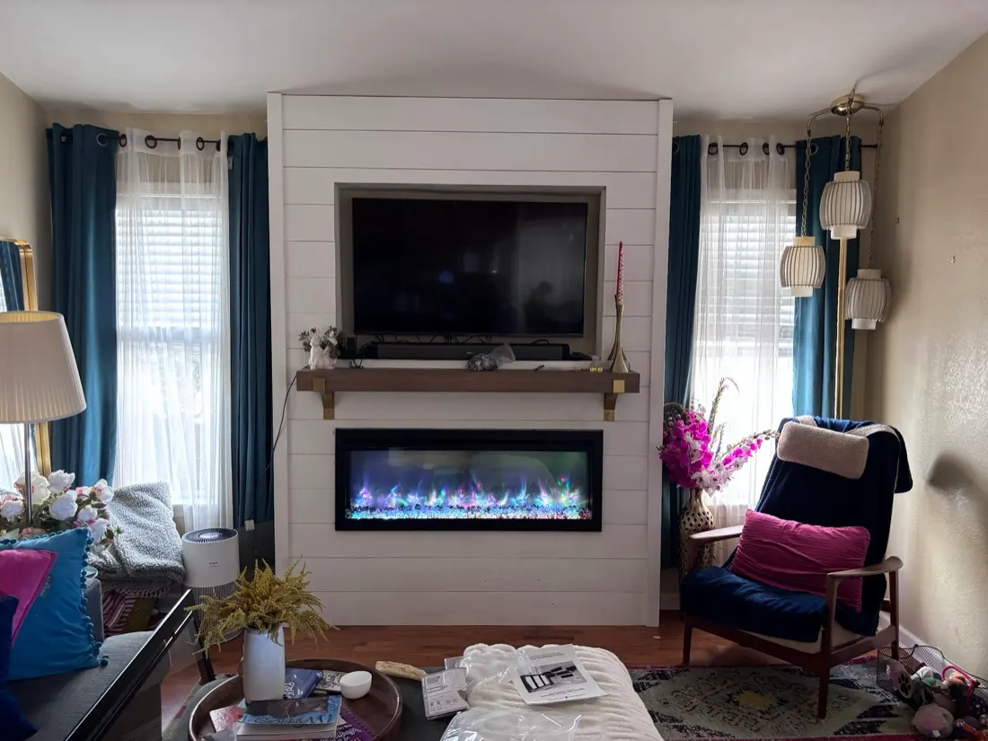 TV recessed into a shiplap wall above an electric fireplace and mantel